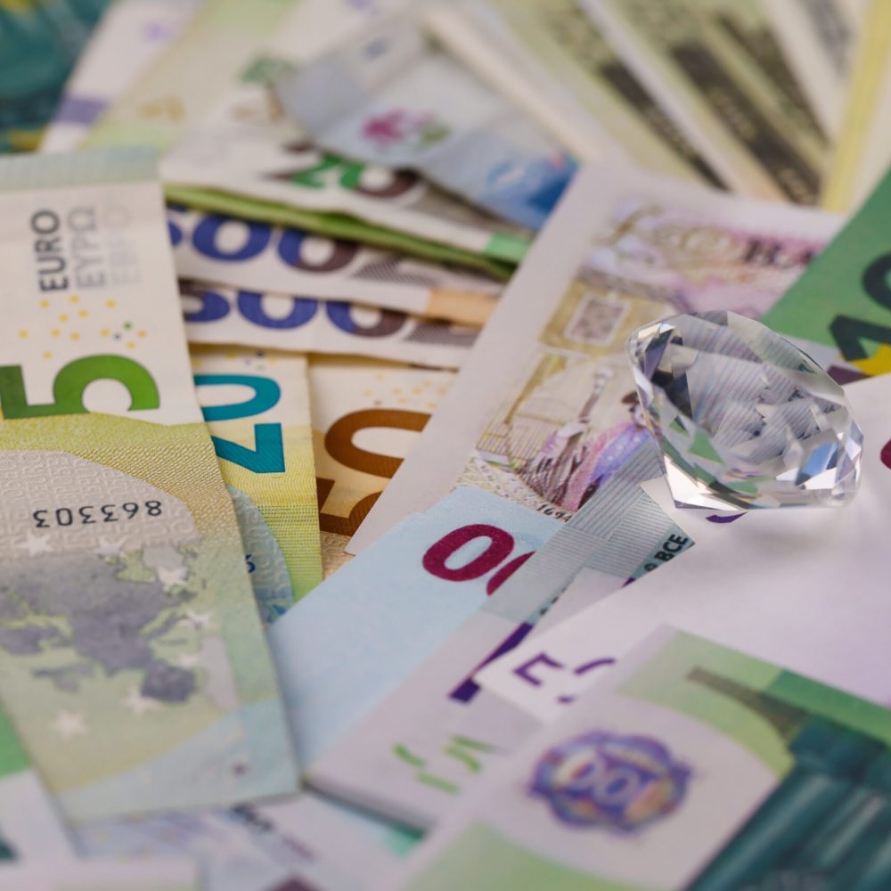 Euro and dollar money bills and coins with large diamond close up. Big amount of money and huge transparent gem on table. Business and jewellery concept